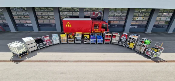 Auf dem Bild ist im Hintergrund das Gerätehaus von der Freiwilligen Feuerwehr Gundelfingen zu sehen. Davor Steht der Gerätewagen Logistik mit Rufname GWL 55/1. Davor stehen alle zwanzig Rollcontainer in einem Halbkreis aufgestellt.