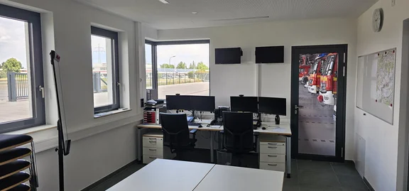 Raum mit 2 Schreibtischen mit jeweils einen Funkgerät sowie je einen Computer. Desweiteren ein Besprechungsplatz sowie mehrere Whiteboards für Darstellung von Einsatzlagen, Karten etc.
